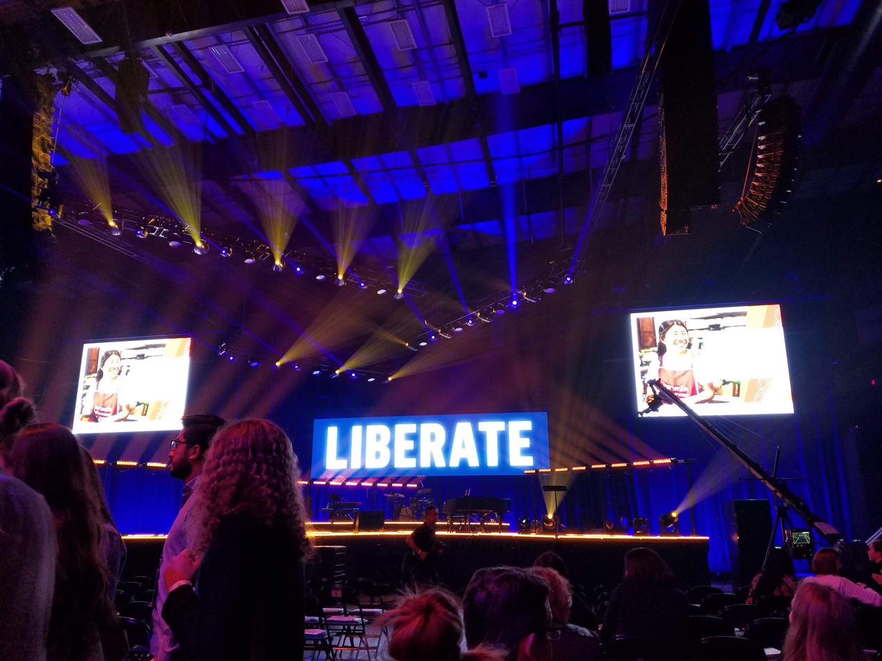 A conference stage bathed in blue light with a large illuminated LIBERATE sign